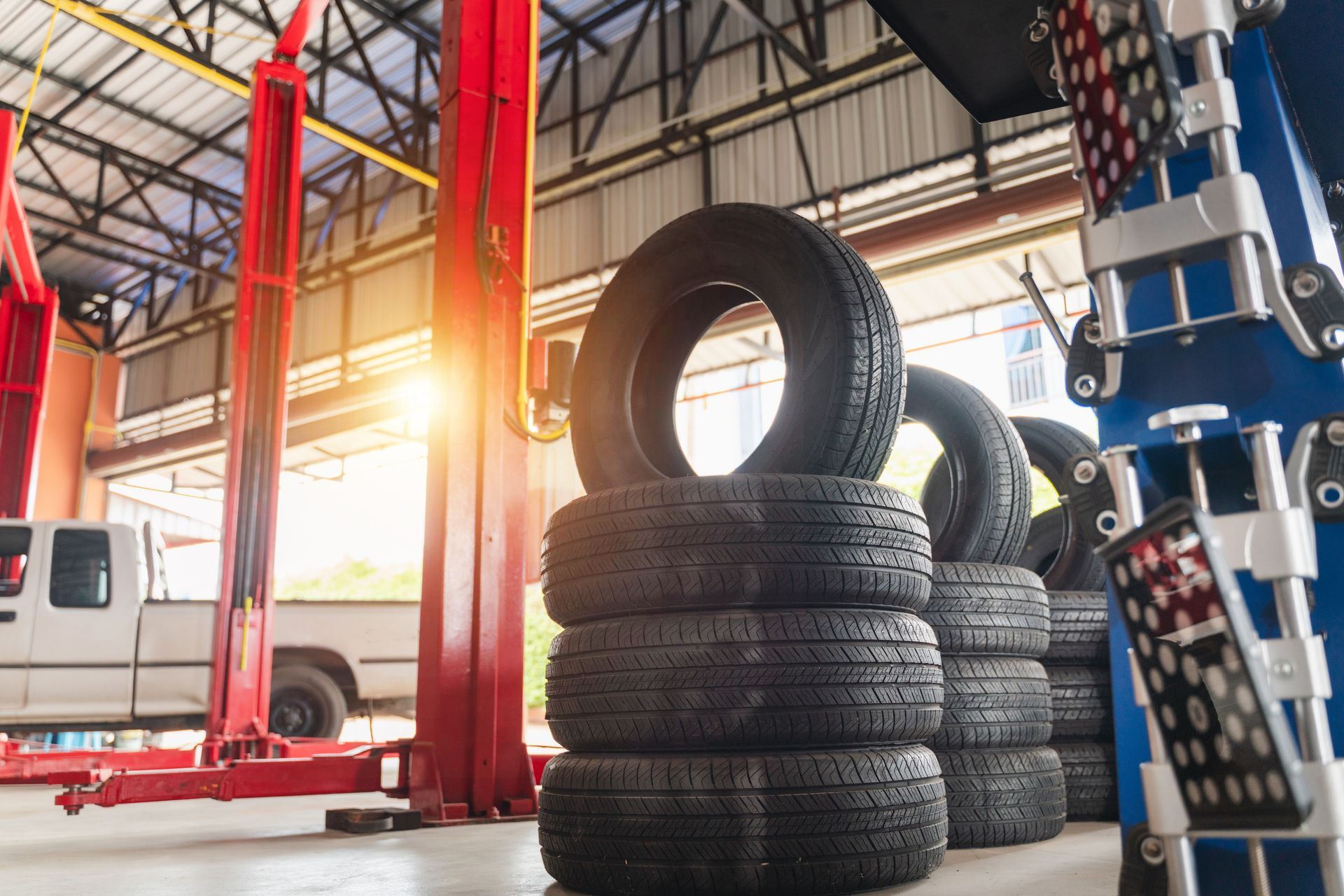 Auto repair shop with stacks of tires and red vehicle lifts under a bright industrial roof