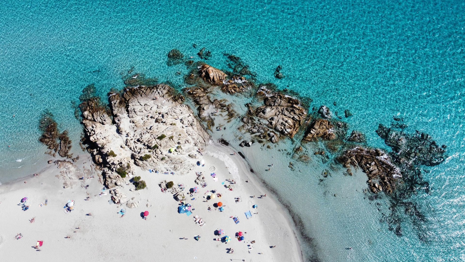 Weisser Sandstrand mit türkisfarbenem Wasser, Felsvorsprung, sonnenbadende Menschen.