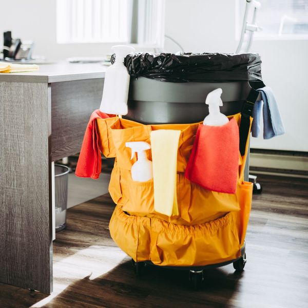 A yellow cleaning cart with cleaning supplies in the pockets