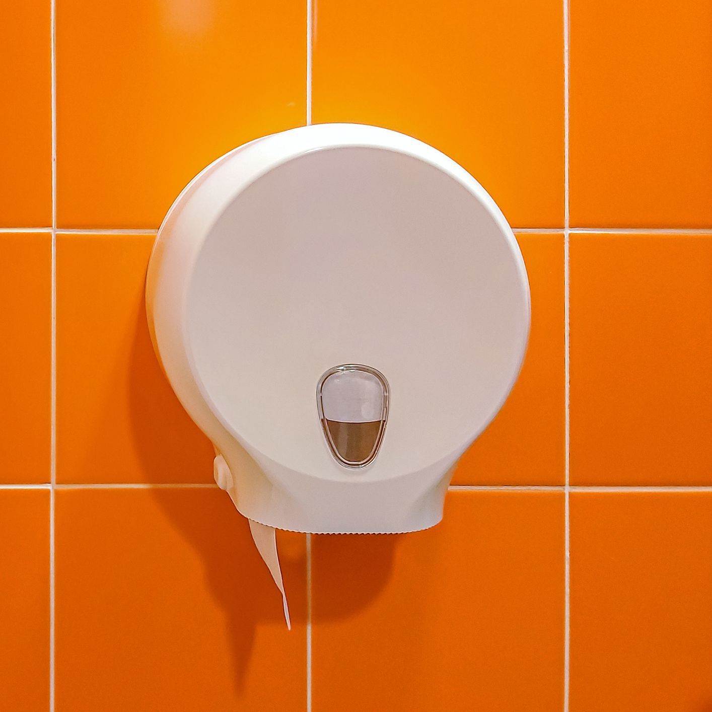 A white toilet paper dispenser on an orange tiled wall