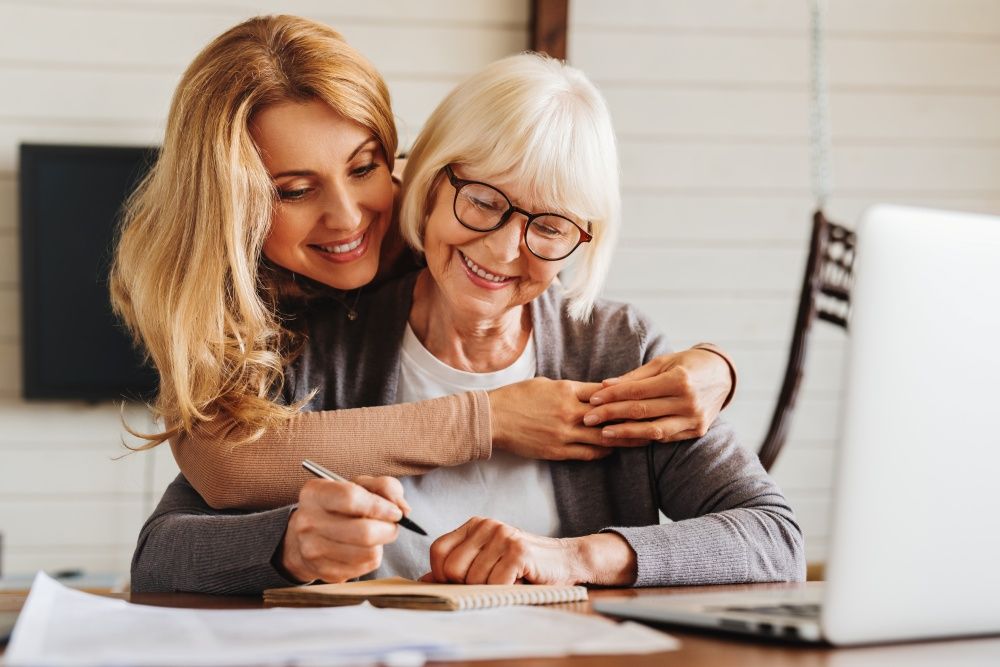 A Woman Is Hugging An Older Woman While Sitting At A Table — O'Reilly & Sochacki Lawyers in Murwillumbah, NSW