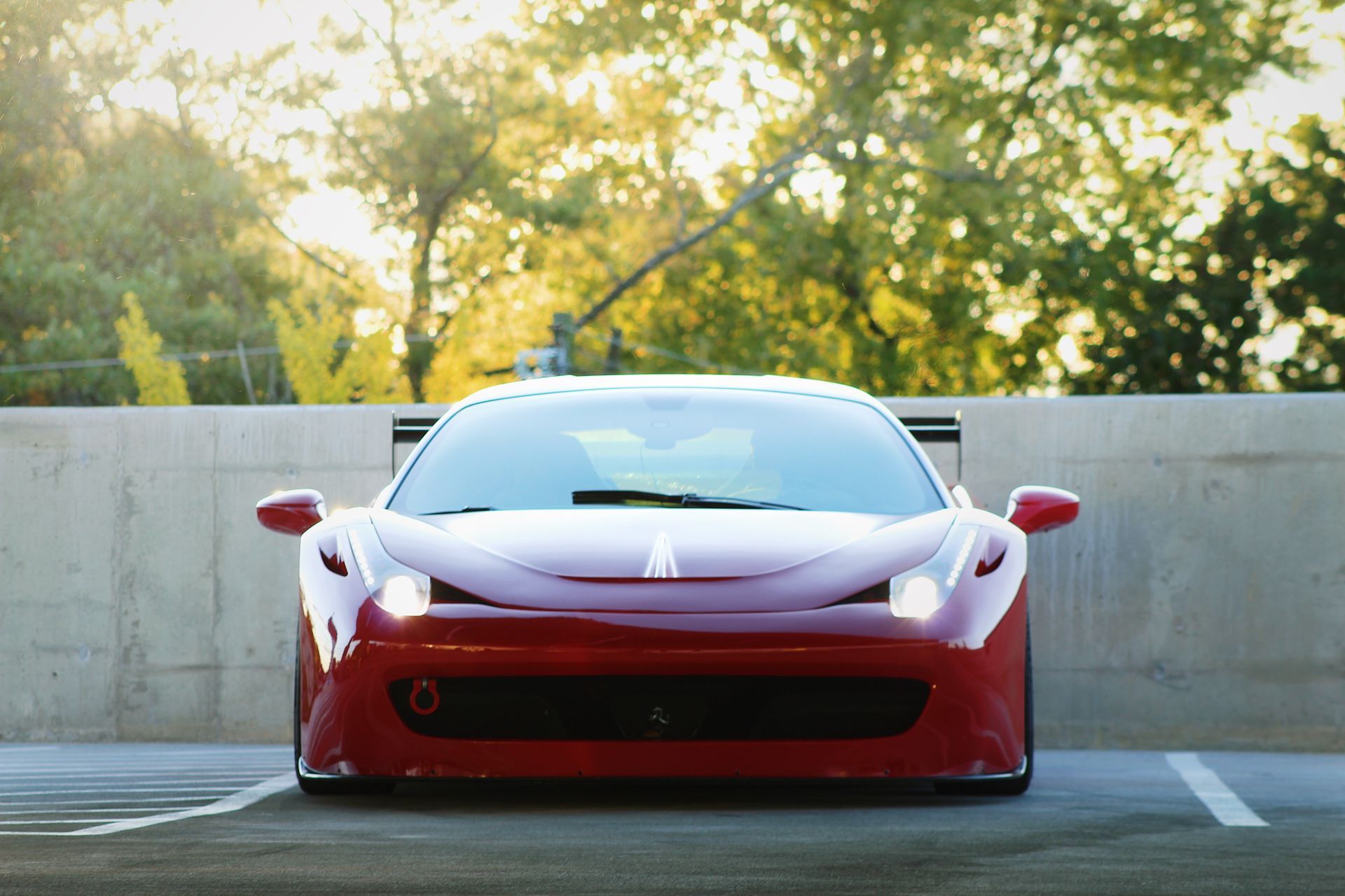 Red Ferrari sports car parked in front of a concrete wall, sunlight in the background.
