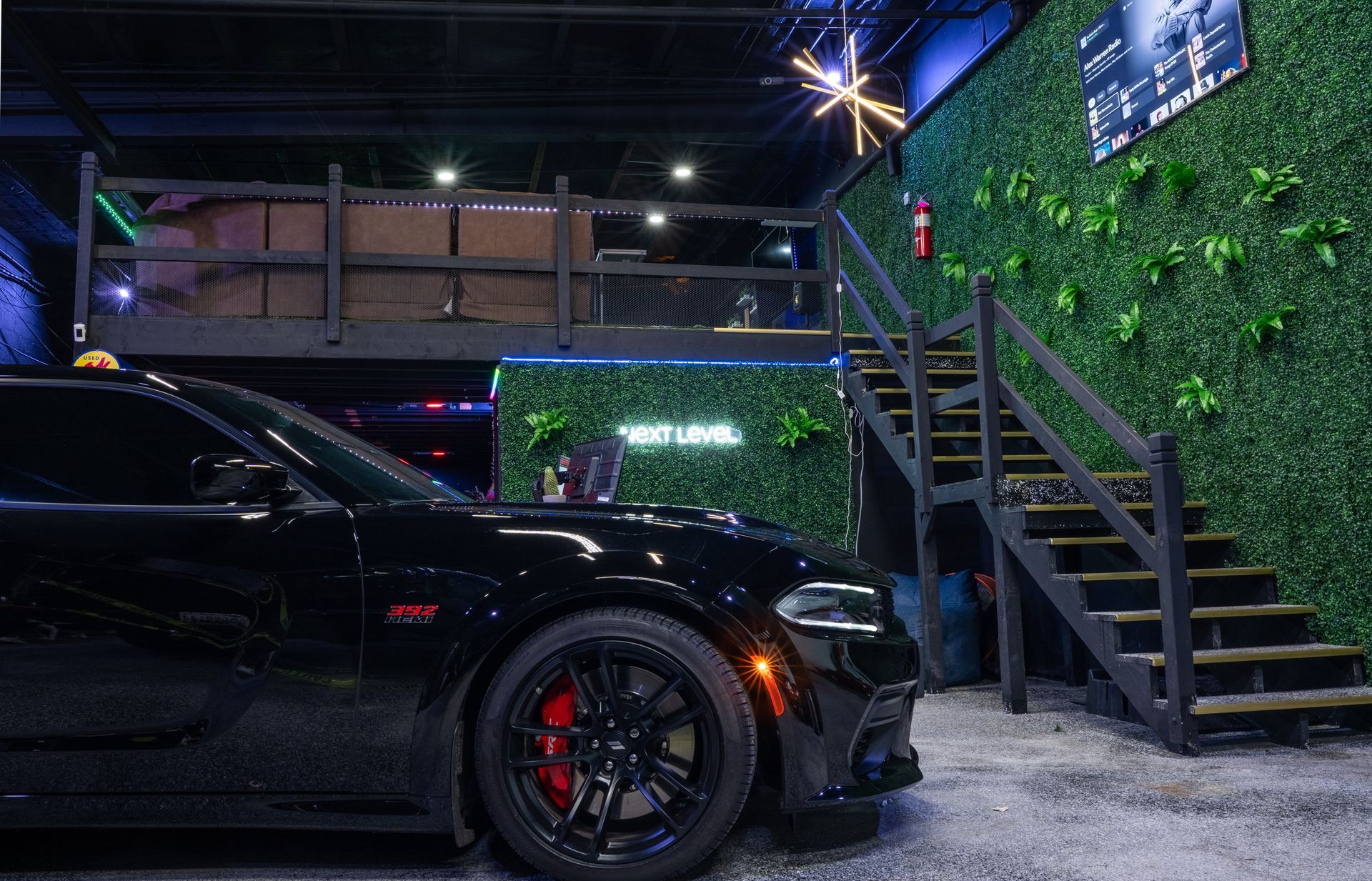 Black car parked in front of a venue with stairs, green wall, and neon sign.