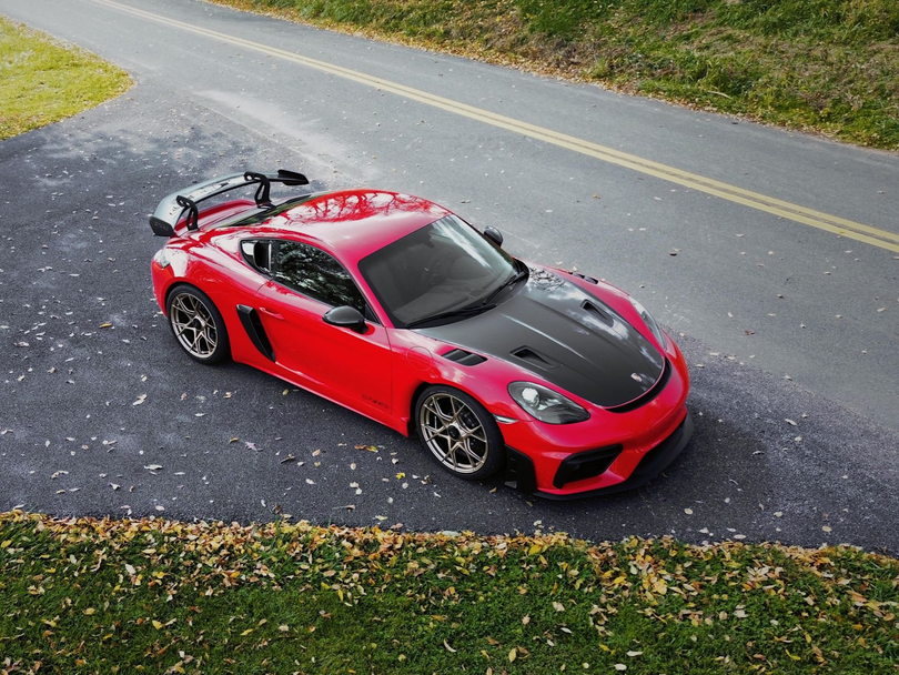 A person uses a racing simulator with multiple screens in a dark room. A dog rests on the floor nearby.