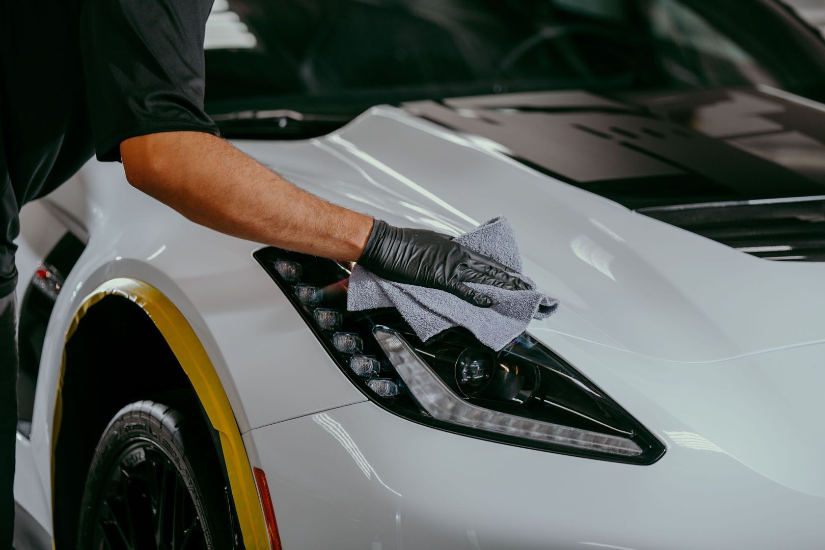 A man is cleaning a white sports car with a towel.