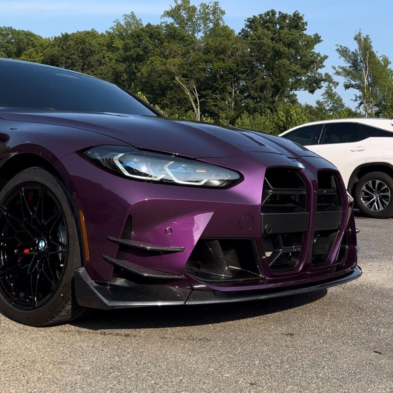 Purple BMW M4 with black wheels and a front spoiler; a white SUV is in the background.