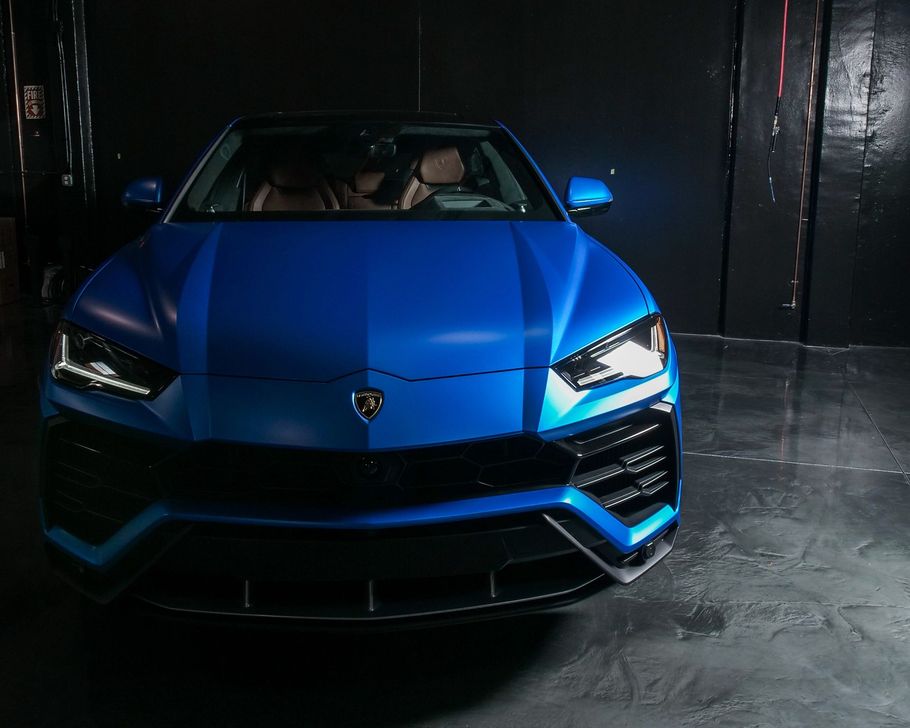 A blue lamborghini urus is parked in a dark garage. 