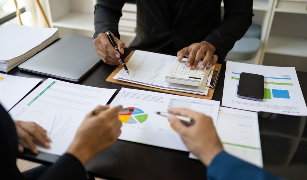 People reviewing financial documents at a desk, using a calculator and pointing at charts.