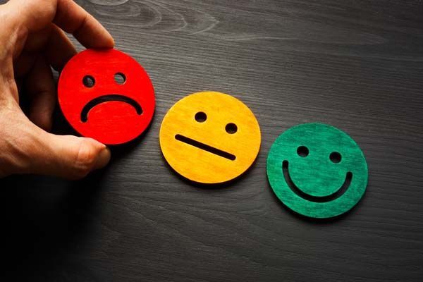 Hand placing a red sad face token beside yellow neutral and green smiling face tokens on a dark table