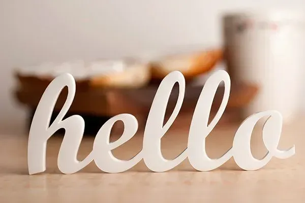 White cursive “hello” sign on a blurred tabletop with a mug in the background
