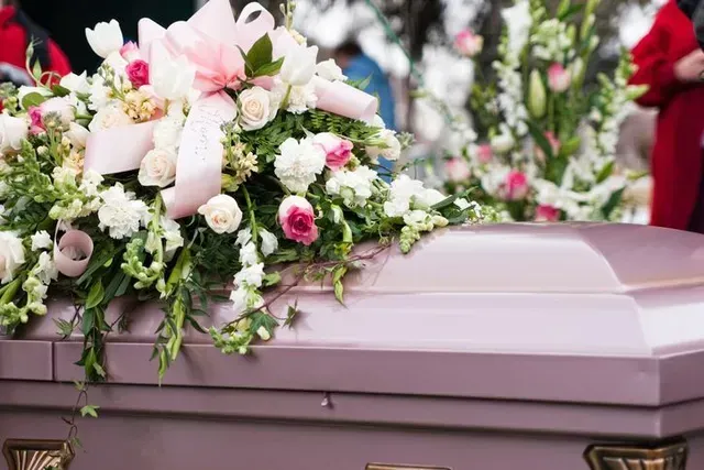 Pink casket adorned with white and pink funeral flowers at a memorial service
