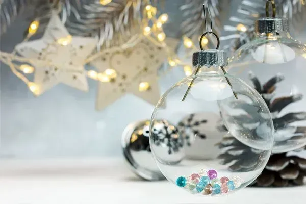 Clear glass Christmas ornaments with silver pinecones and warm fairy lights on a white surface