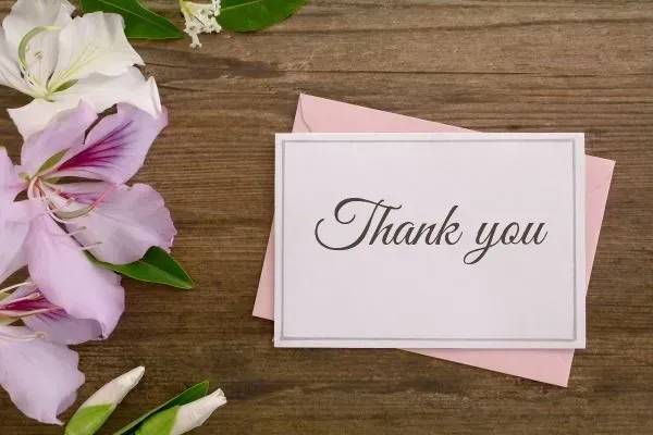 Thank-you card on a wooden table with pink flowers and envelope background