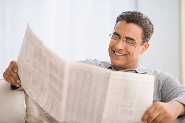 Man smiling while reading a newspaper on a couch