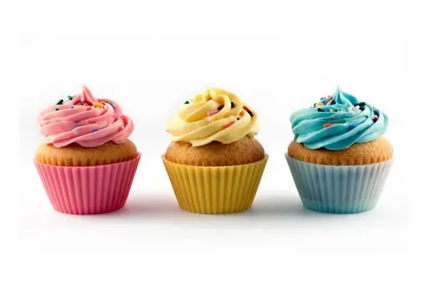Three frosted cupcakes in pink, yellow, and blue wrappers on a white background