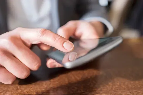 Finger tapping a smartphone screen on a wooden table