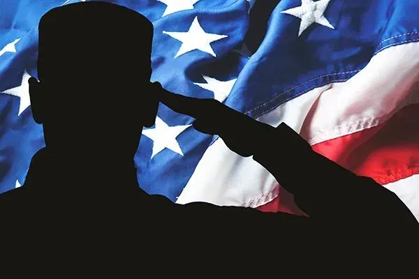 Silhouette of a saluting military figure before a waving American flag