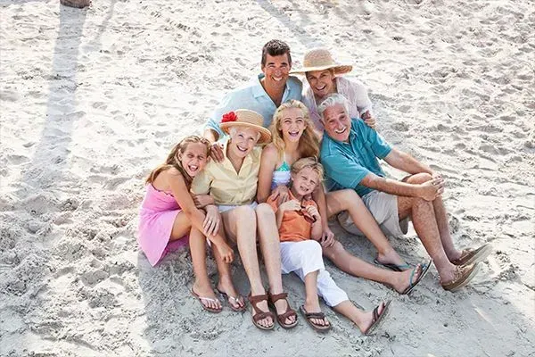 Group of people sitting closely together on a sandy beach, smiling and relaxing in colorful clothes.