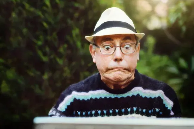 Man in a white hat and glasses making a surprised face against a blurred green background