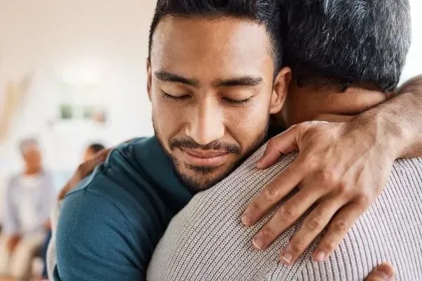Two people embracing warmly indoors, one with eyes closed and a calm expression