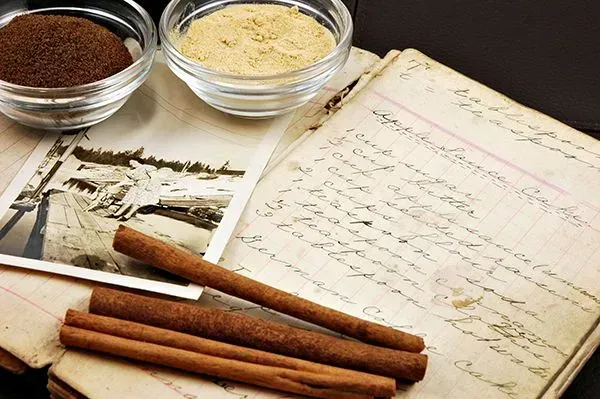 Open recipe book with cinnamon sticks, spice bowls, and a vintage black-and-white photo on a table