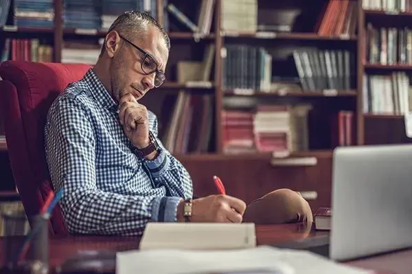 Person writing at a library desk with bookshelves in the background