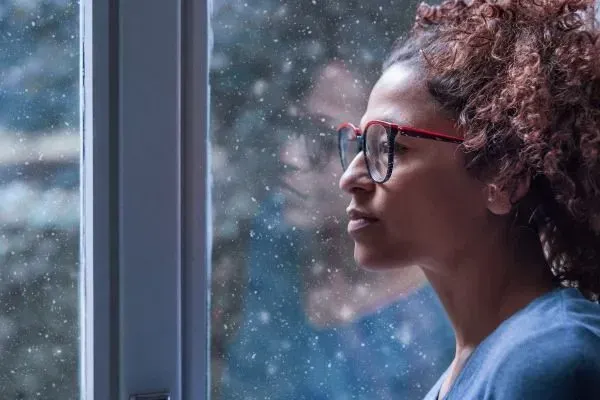 Woman in red glasses looking out a window on a rainy day