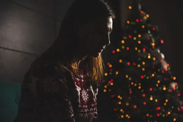 Silhouetted person beside a lit Christmas tree in a dark room