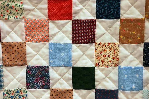 Patchwork quilt with multicolored fabric squares in red, blue, cream, and floral patterns