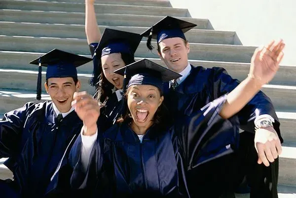 Graduates in blue caps and gowns smiling and waving on outdoor steps