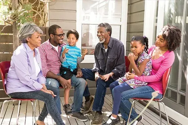 Family seated and talking on a porch, with two children and colorful casual clothing