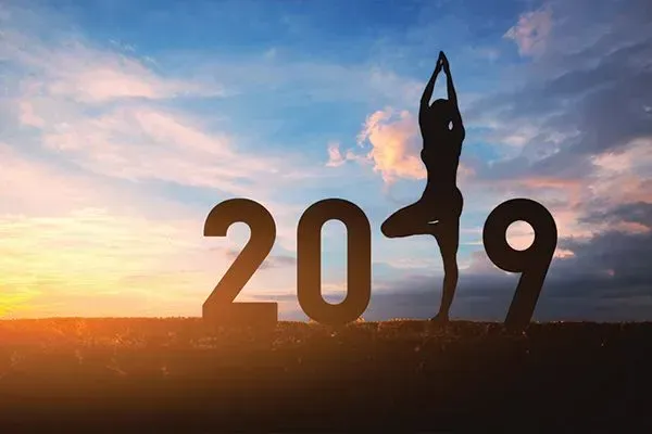 Silhouette of a person in a yoga pose inside the number 0 of “2019” at sunset with a colorful sky