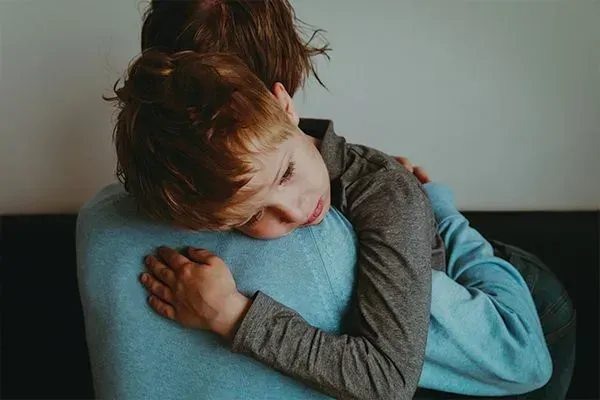 Two children hugging closely, one in a gray sweater and one in a blue shirt