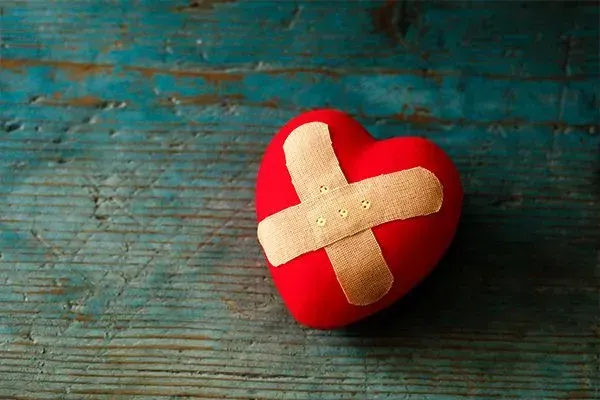 Red heart-shaped object with a beige cross on a teal wooden surface
