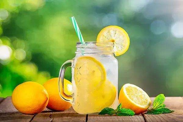 Fresh lemon juice in a mason jar with lemons and mint on a wooden table outdoors