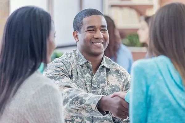 Smiling soldier in camouflage shakes hands during a conversation with two people indoors
