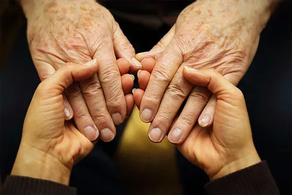 Two pairs of hands gently touching, one older pair above and one younger pair below