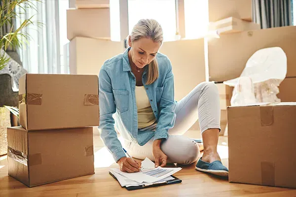 Woman packing boxes and filling out paperwork on the floor in a bright moving room