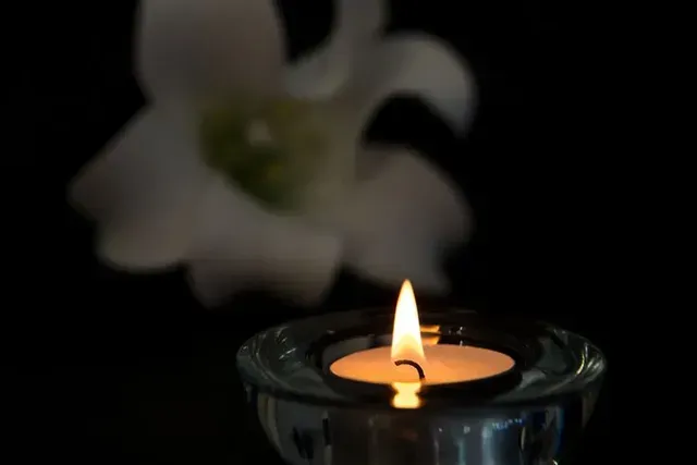 Lit candle in a glass holder with a blurred white flower in the background