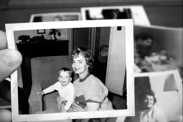 Hand holding a black-and-white snapshot of a smiling woman with a baby indoors