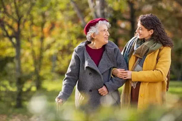 Two people walking arm in arm in a park, smiling and wearing autumn coats and scarves.