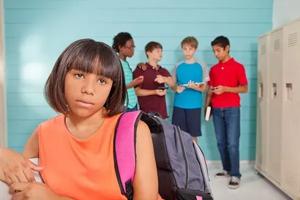 Student with backpack in a school hallway, looking concerned while classmates stand by lockers.