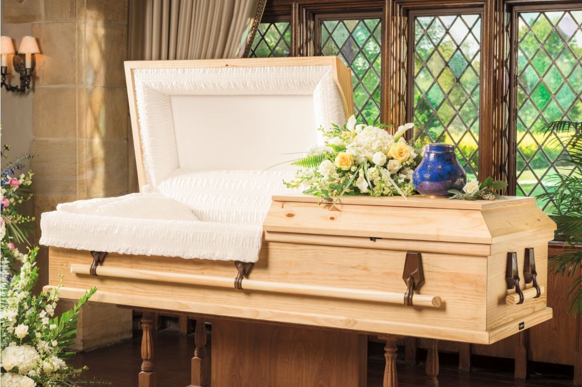 Coffin-shaped wooden bench with white cushion and flowers in a sunlit room