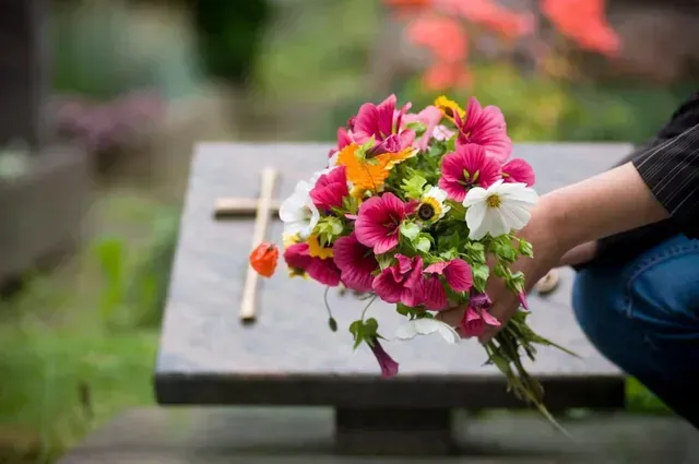 Bouquet of pink, white, and yellow flowers held beside a stone bench in a garden.