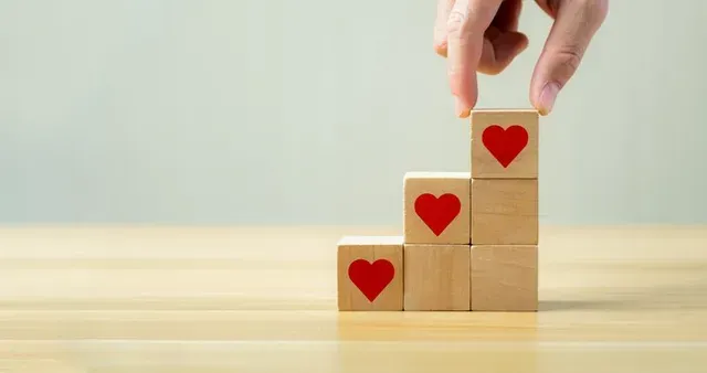 Hand placing a wooden block with red heart on a stepped stack of heart blocks