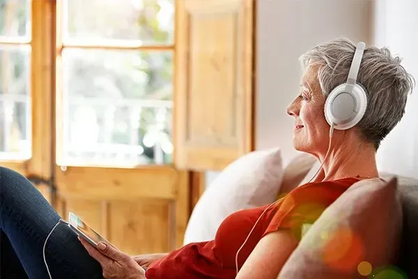 Person wearing white headphones relaxing on a couch by a bright window in a cozy room