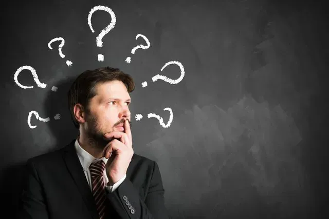 Man in a suit thinking in front of a chalkboard with question marks overhead