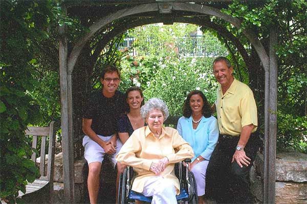 Five people pose in a garden arbor, with an elderly woman seated in front.