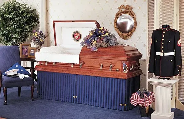 Open casket funeral display with flowers, framed portrait, and uniformed guard beside it