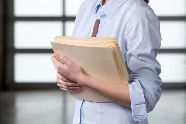 Person in a white shirt holding a tan file folder in a bright office hallway